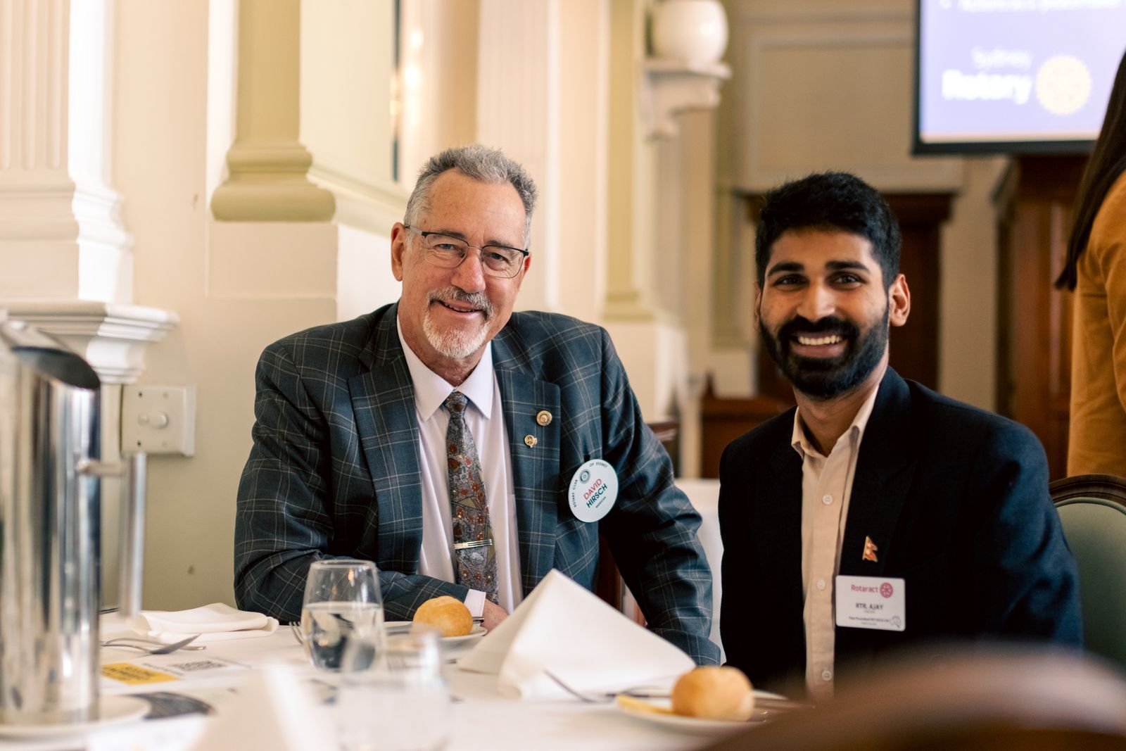Ajay in conversation with an older man at a formal lunch table.